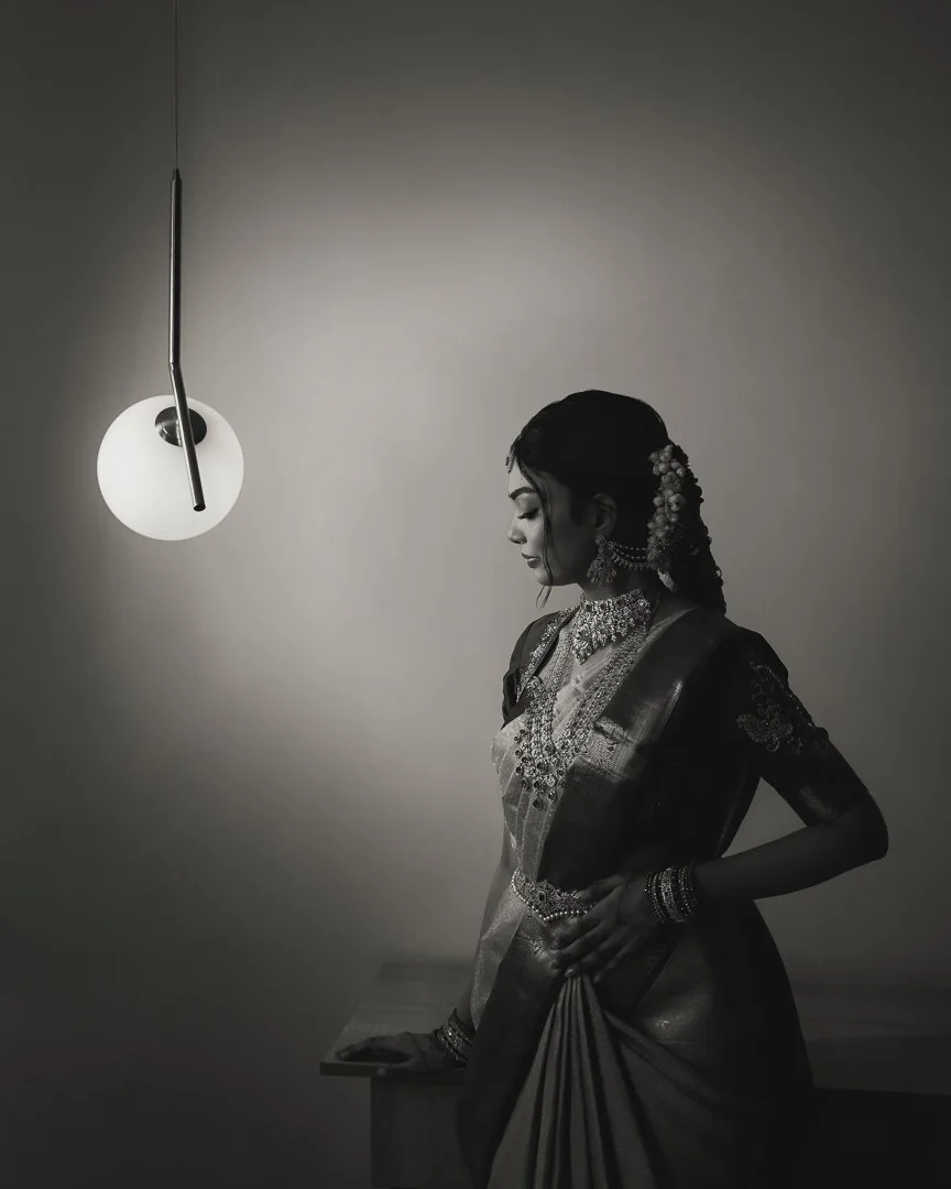 A bride beside a hanging pendant light, photographed in black and white