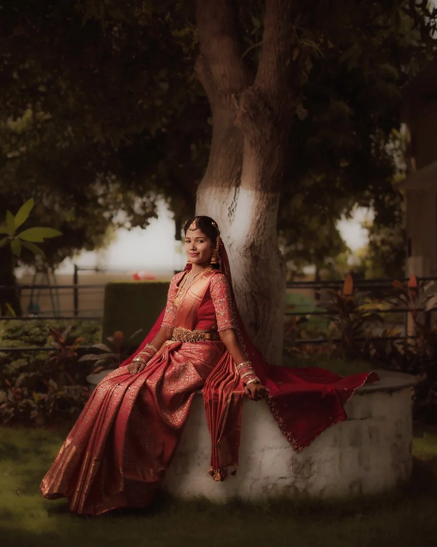 A woman in a red sari seated beneath a tree