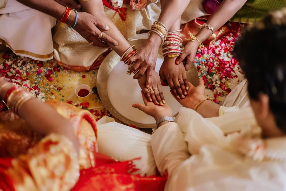 Several hands gathered over ceremonial flowers and a tray